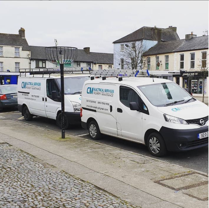 Two CM Electrical Services vans with their blue livery, parked in a town square