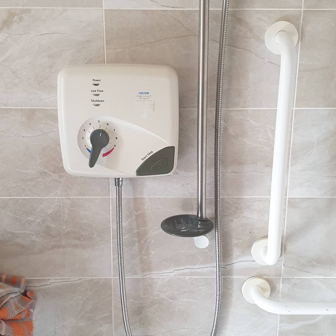 An electric shower on a tiled wall beside a grab rail