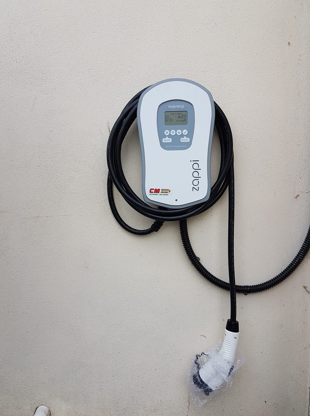 A wall-mounted EV charger with a CM sticker
